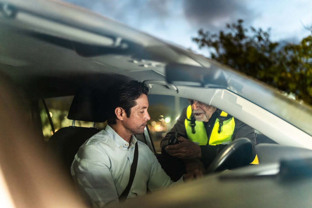 A man sitting in his car being questioned by a police officer in a yellow vest, representing a field sobriety test scenario in New York.