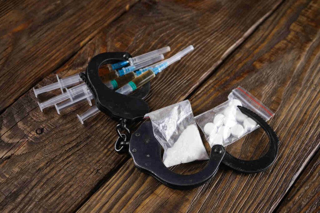 Handcuffs, syringes, and bags of pills on a wooden table, symbolizing DWI charges related to prescription medications.