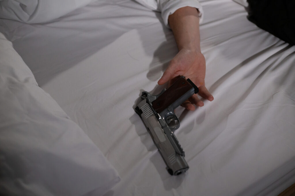 Commit the Killing but Still Face Life. In This Image a person is lie on the bed with holdig gun on hand