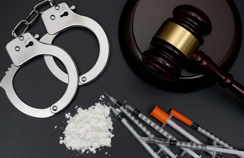 Close-up of handcuffs, a gavel, syringes, and a pile of white powder, symbolizing drug charges and legal proceedings in New York drug cases.